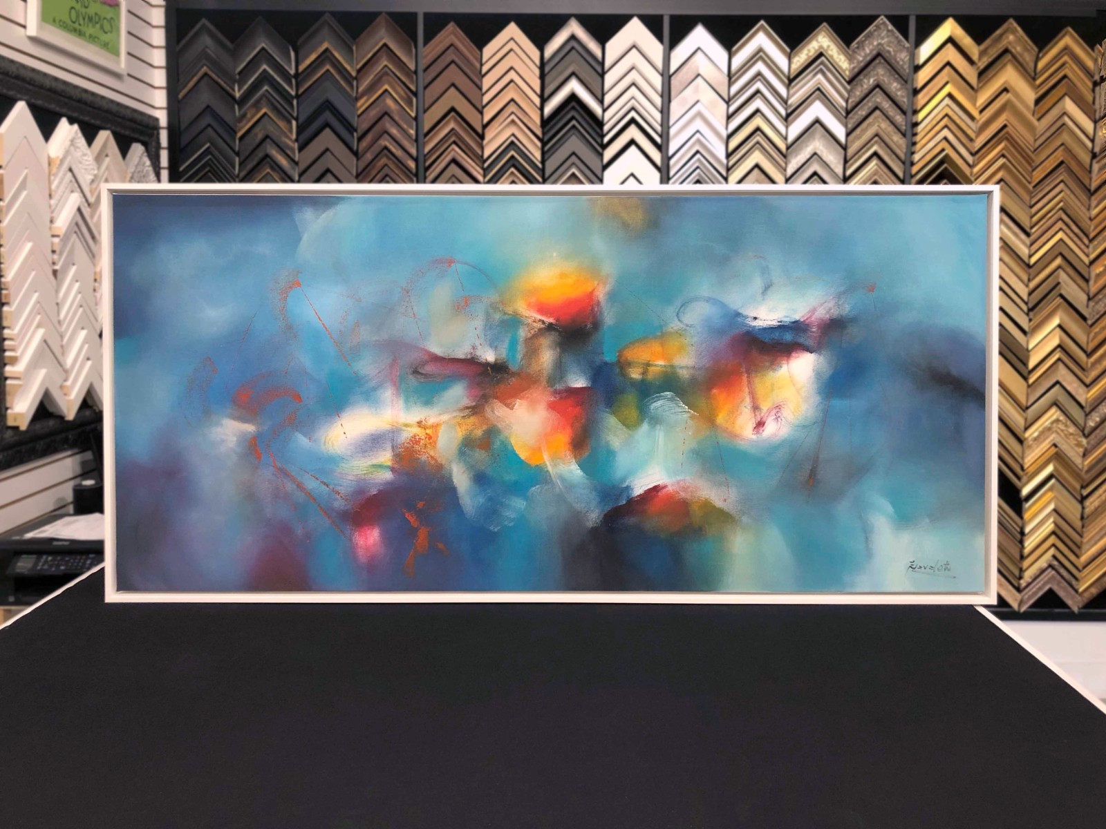 Finished framed abstract on the counter, moulding samples behind.