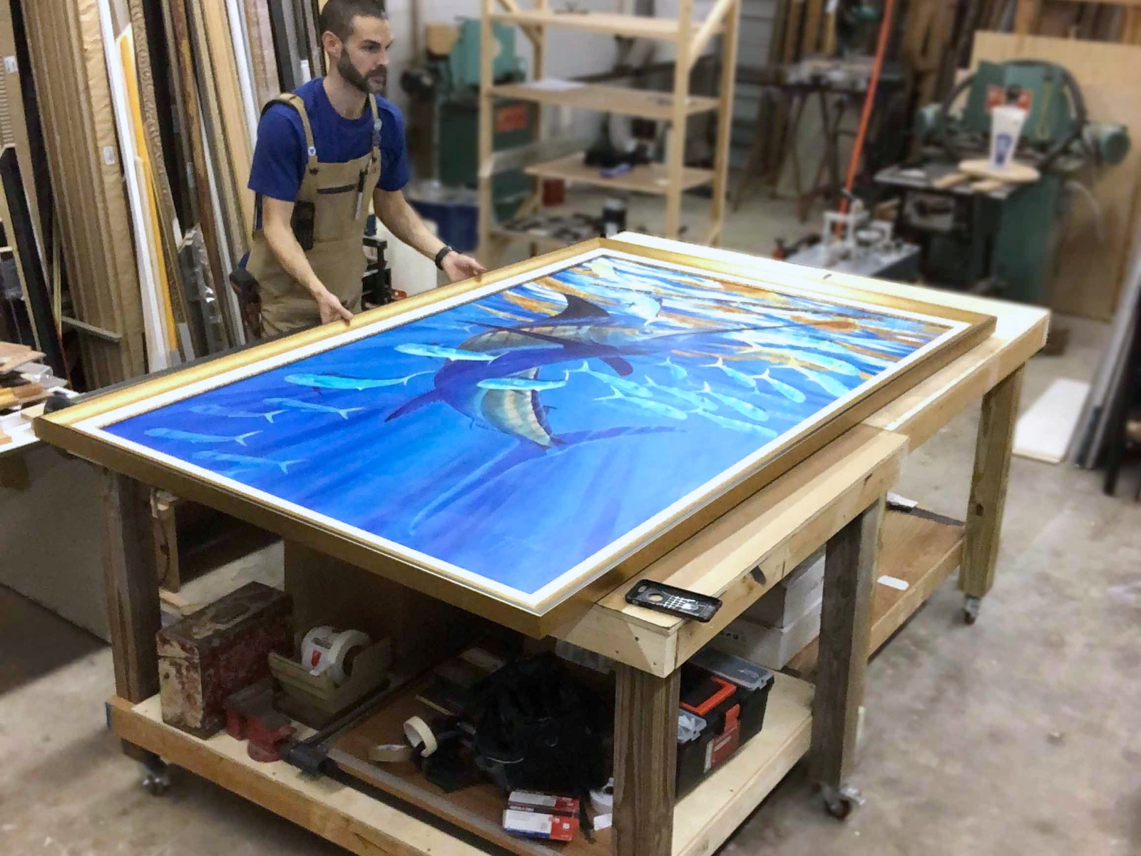 A framer at the bench with a large marine canvas, the moulding wall behind.